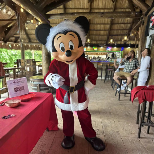 Mickey Mouse mascot in Santa suit greeting guests at a restaurant holiday party, Christmas character rental for Miami businesses.
