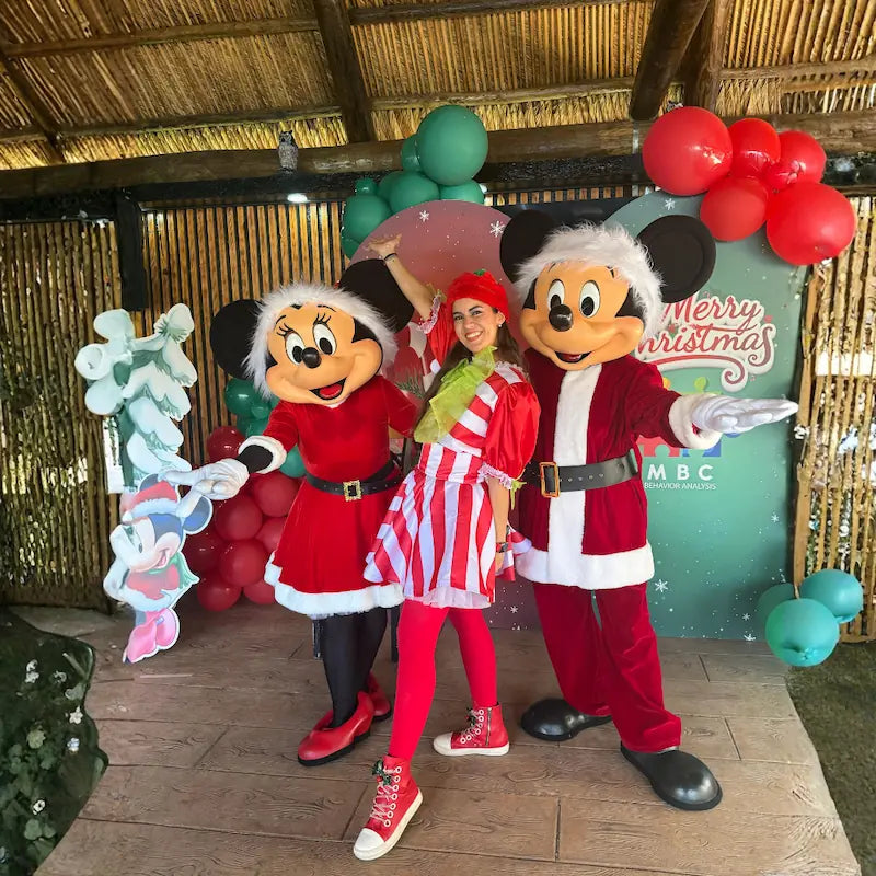 Santa Mickey and Minnie with a candy cane host in front of a Merry Christmas branded backdrop, holiday trio by Fantasy Entertainments.
