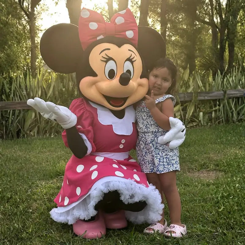 Minnie Mouse mascot hugging a little girl at golden hour, a tender character experience moment at a Miami backyard birthday.