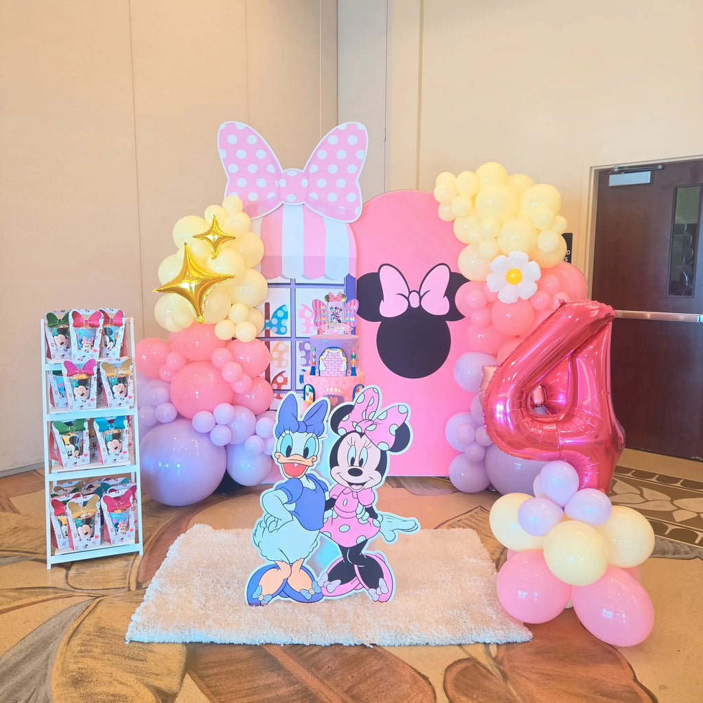 Full Minnie Mouse birthday party setup with Daisy and Minnie cutouts, favor stand, pastel balloon garland and bow backdrop in a Miami hotel ballroom.