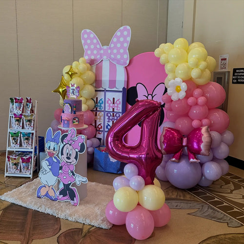 Minnie Mouse party decoration with pink balloon arch, bow backdrop, number 4 foil balloon, cake pedestal and favor stand at a Miami hotel venue.