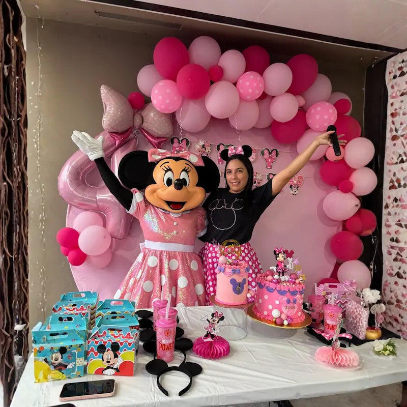 Minnie Mouse character and host with microphone in front of a pink balloon arch and dessert table, all inclusive party package in Miami.