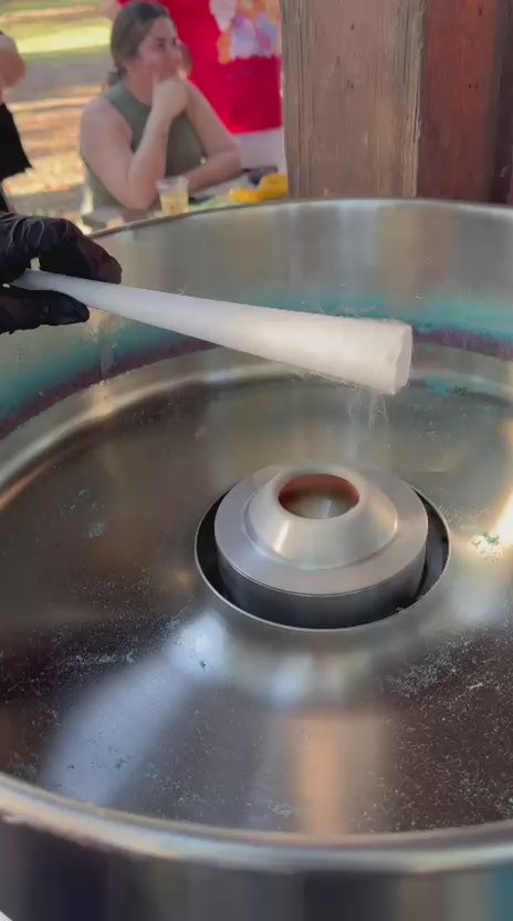 Close-up video of a gloved attendant rolling a fresh cotton candy cone over the spinning bowl at an outdoor Miami event.
